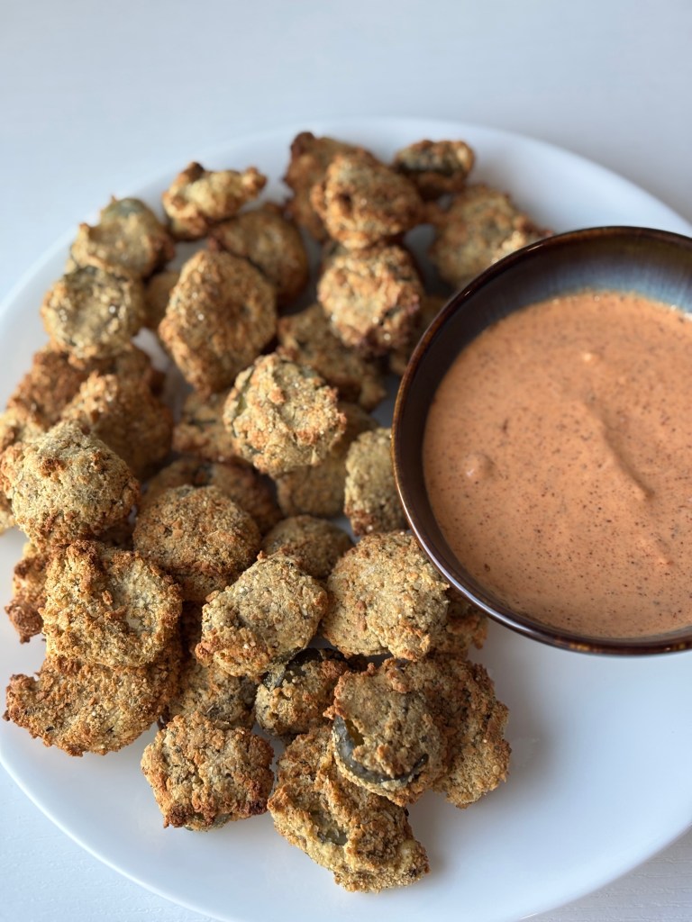 A plate of crispy baked okra served with a small bowl of dipping sauce.